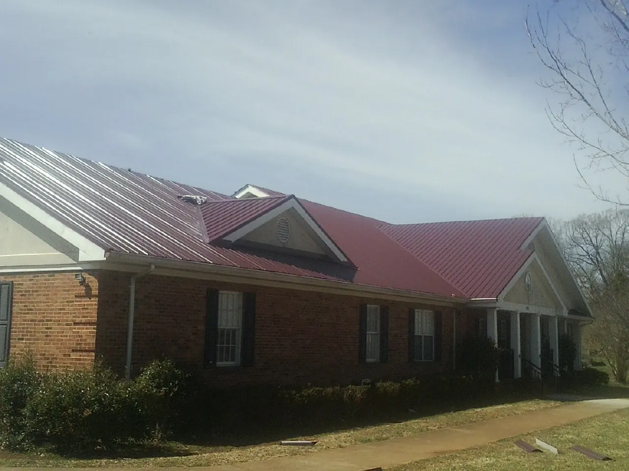 Red metal roof with gabled entries on a long brick building, from a Hail Damage Roof Repair job in Woodlyn