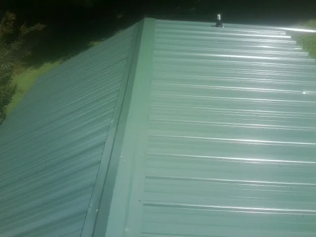 New green metal panels meeting at the ridge of a roof — Flat Roof Repair work by our crew in Woodlyn