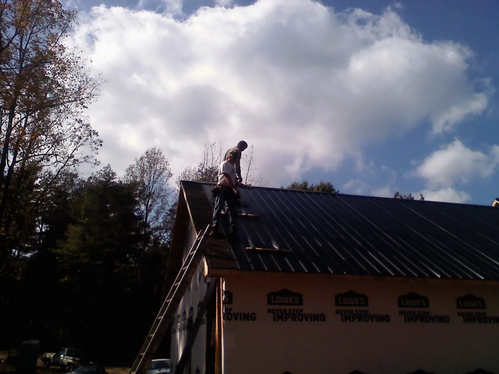 Roofer fastening dark metal panels high against a cloudy sky, from a Roof Inspection job in Woodlyn