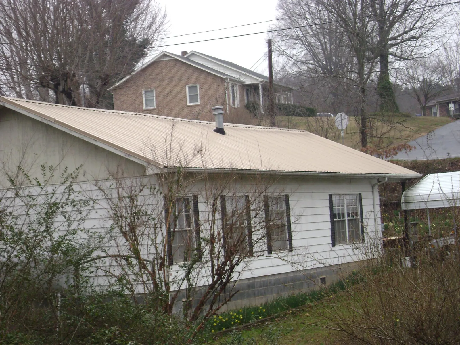 Tan metal roof on a white sided house set into a hillside — Commercial Roofing by Roofing Brothers in Woodlyn