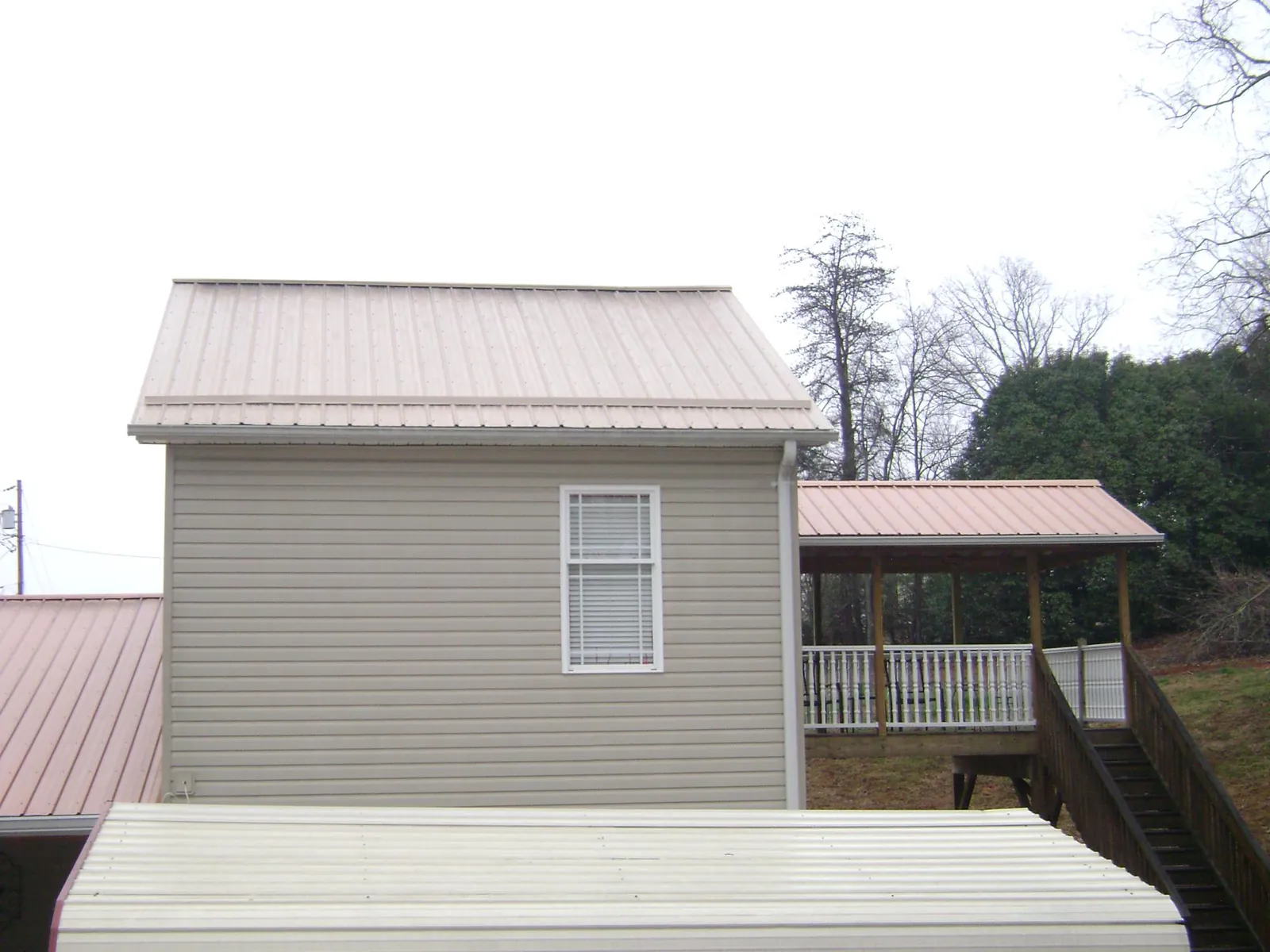 Tan metal roofs on a two story addition and attached porch, from a Roof Replacement job in Woodlyn